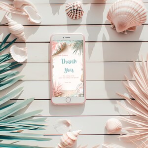 Puede incluir: Un tel&eacute;fono inteligente rosa muestra una tarjeta de "Gracias" con un tema de playa, rodeada de conchas marinas y hojas de palma sobre una superficie de madera blanca. La tarjeta presenta texto e ilustraciones de conchas y plantas.