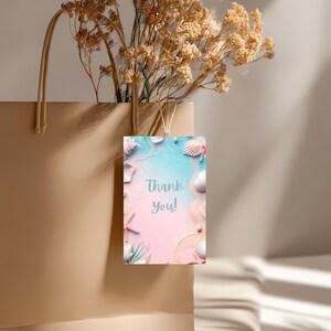May include: A beige paper shopping bag with dried flowers and a tag that says "Thank you!" The tag has a beach theme with seashells, starfish, and a pink and blue background.