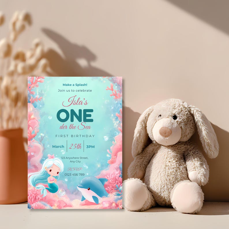 Baby girl’s mermaid first birthday invitation standing beside a soft plush bunny, with aqua water, pink coral and a cute dolphin.