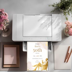 Printed elegant mens birthday invitation coming out of a printer, showcasing minimalist gold design with seated man illustration and clean modern typography