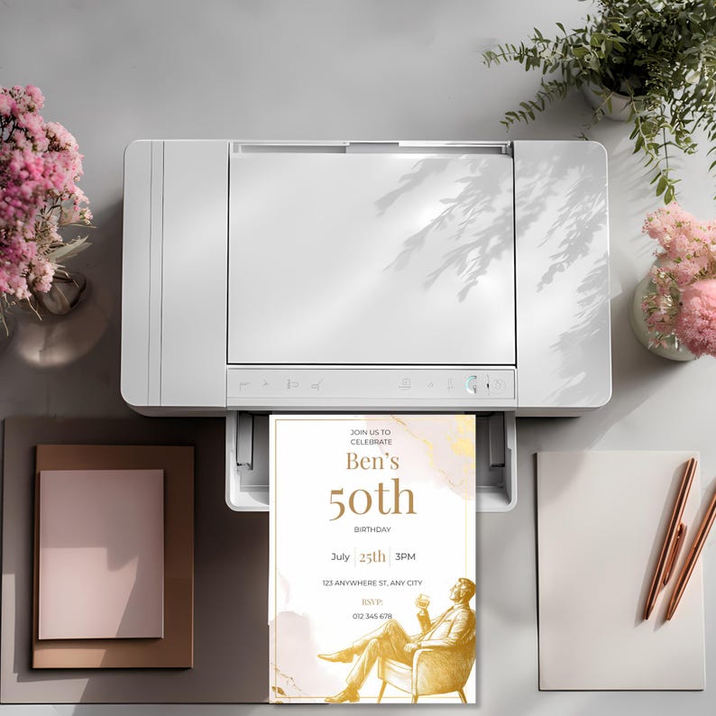 Printed elegant mens birthday invitation coming out of a printer, showcasing minimalist gold design with seated man illustration and clean modern typography