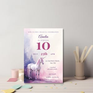 Elegant purple unicorn birthday invitation for girls leaning against a gray wall on a pastel desk