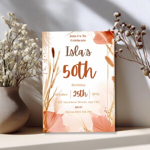 Boho terracotta 50th birthday invitation card leaning against a wall beside a vase of dried flowers
