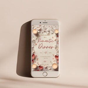 May include: A smartphone displays a romantic dinner invitation. The design features a cream-colored background with red hearts, white flowers, and lit candles. The text reads "You're Invited!! To A Romantic Dinner" with date and time details.