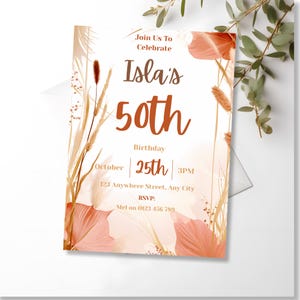 Angled close-up of the boho birthday invitation styled with green leaves on a light backdrop