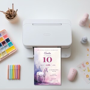 Unicorn birthday invitation printing from a white home printer on a desk with pastel markers and a watercolor paint palette