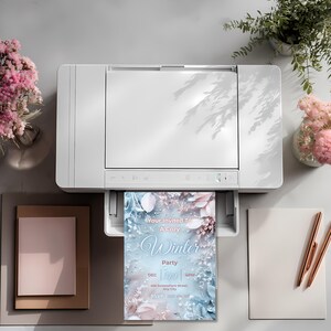 May include: A white printer printing a winter party invitation. The invitation has a blue and pink floral design with the text "Your Invited To A Cozy Winter Party". The scene includes flowers, stationery, and pens.