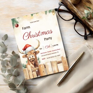 Rustic farm Christmas party invitation with a highland cow in a Santa hat on a whitewashed wooden desk with eucalyptus, glasses and a gold pen
