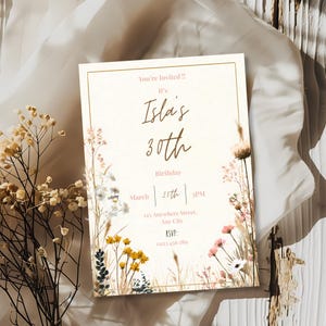 May include: A cream-colored invitation with a gold border, featuring floral illustrations and the text "You're Invited!! It's Isla's 30th Birthday March 25th 3PM". Includes address and RSVP information. Decorative floral elements.