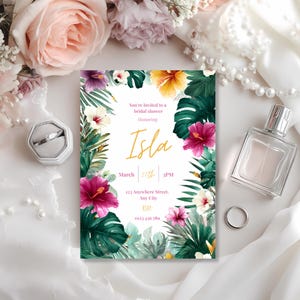 May include: A bridal shower invitation featuring a floral design with pink, yellow, and white hibiscus flowers and green tropical leaves. The invitation text reads "You're invited to a bridal shower Honoring Isla" with the date and time. A ring and perfume bottle are also visible.