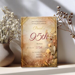Styled flat lay, dried white flowers
Elegant 95th birthday invitation template in warm amber and gold Art Deco style, displayed as a printed card standing upright beside a vase of dried white flowers and cotton stems