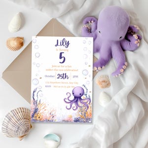 May include: A birthday party invitation with an under-the-sea theme, featuring an illustration of an octopus and aquatic plants. A plush purple octopus and seashells are arranged around the invitation. The invitation is for a child's fifth birthday.