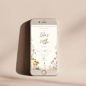 May include: A smartphone displays a digital invitation for Isla's 30th birthday. The invitation features floral accents, the text "You're Invited!!", and details for the event on March 25th at 3 PM. The phone is set against a neutral background.