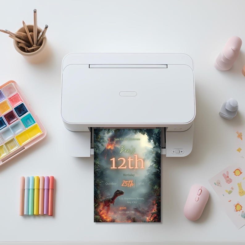 May include: A white printer is printing a birthday invitation with a dinosaur theme. The invitation reads "Ben's 12th Birthday" with the date October 25th. Other items on the white surface include art supplies and a pink mouse.