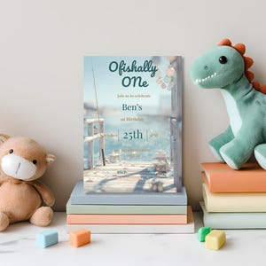 Printed fishing-themed 1st birthday invitation presented as a clean flat lay showcasing “Ofishally One” design with coastal celebration styling.