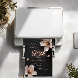 Printable black floral 25th birthday invitation template coming out of a home printer, showing how to print your editable Canva invite at home