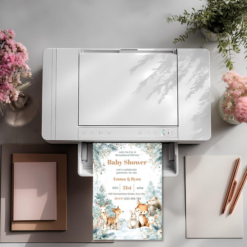 Winter woodland baby shower invitation printing from a home printer, styled with fresh flowers and stationary nearby