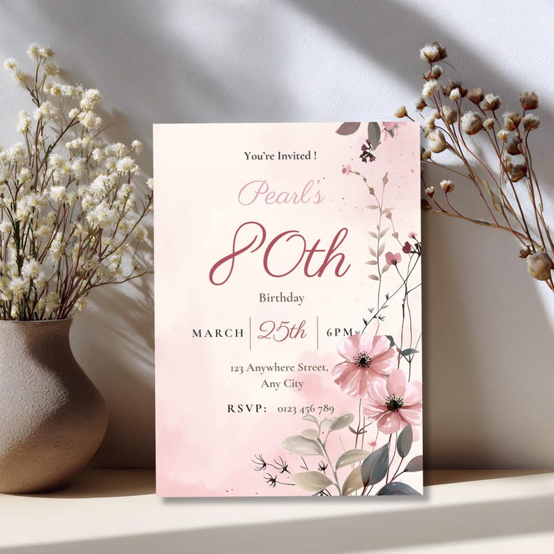 80th birthday invitation card displayed near dried flowers, elegant pink floral watercolor design, editable Canva template