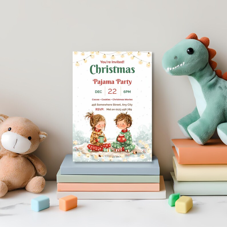Printed kids Christmas pajama party invitation on a stack of books in a child's room, between a teddy bear and a plush dinosaur