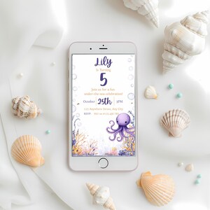 May include: A mobile phone shows a birthday invitation with an underwater theme. The invitation features an octopus and coral illustration, with text reading "Lily is turning 5." Seashells and beads surround the phone, creating a decorative arrangement.