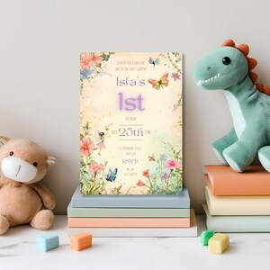 Editable fairy garden birthday invitation standing on a stack of pastel books between a teddy bear and dinosaur plush toy, showing the enchanted garden design with fairy, butterflies and botanical florals