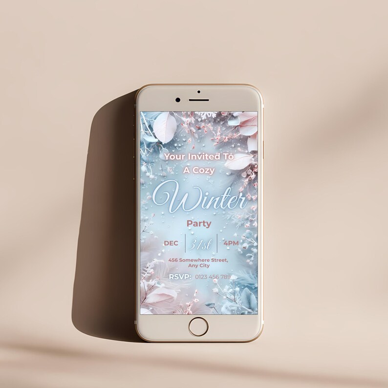 May include: A smartphone displays a winter party invitation. The invitation features a soft blue and pink floral design with the text "Your Invited To A Cozy Winter Party" and event details. The phone is gold-colored.