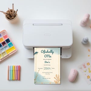 Printed Ofishally One birthday invitation coming out of a printer showing soft coastal fishing themed first birthday design