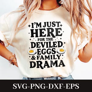 May include: Cream-colored t-shirt with the text "I'M JUST HERE FOR THE DEVILED EGGS & FAMILY DRAMA" in black. The design includes illustrations of deviled eggs. The bottom of the image displays "SVG-PNG-DXF-EPS".