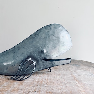 May include: A metal whale sculpture with a gray finish. The whale is in a swimming position with its tail fin raised.