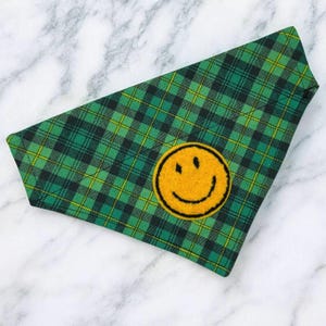 May include: Green and black plaid dog bandana with a yellow smiley face patch.