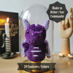 Peut inclure: Figurines de dragon en crochet violet dans un dôme en verre avec une base dorée. Le texte "Make to Order/Sur Commande" et "24 Couleurs/Colors" est visible sur l'image.