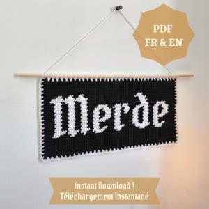 May include: A black and white crochet wall hanging with the word "Merde" in white gothic lettering. The banner is suspended from a wooden dowel and has a white crochet border. The image also includes text that says "PDF FR & EN" and "Instant Download!"