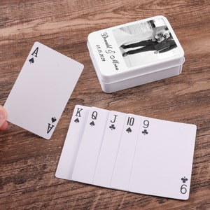 May include: A white rectangular metal tin featuring a black and white photograph of a couple, with the text Donald & Mona 03.15.2024, accompanied by a deck of playing cards showing an ace of spades and a sequence of king, queen, jack, ten, nine, six.