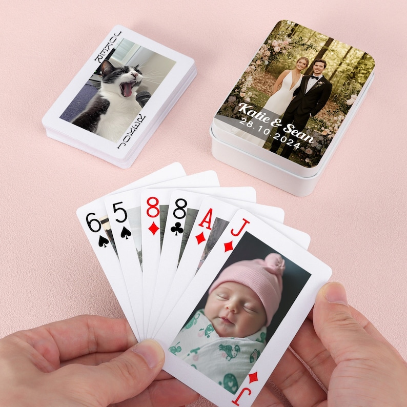 May include: A set of playing cards with a photo of a baby on the Jack of Diamonds card. The cards are fanned out in a hand. The back of the cards are white with a black spade design.
