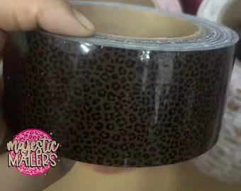 May include: A roll of packing tape with a leopard print design. The tape is brown with black spots and has a glossy finish. The logo "Majestic Mailers" is visible in the lower left corner.