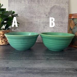 Puede incluir: Dos cuencos de cerámica turquesa con detalles acanalados. Los cuencos son redondos con un borde ligeramente ensanchado. Los cuencos están sobre una superficie de madera oscura. El fondo es una pared gris claro.