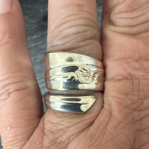 Può includere: Un anello d'argento realizzato con un cucchiaio, con un motivo floreale. L'anello è realizzato con un cucchiaio riutilizzato, con il manico avvolto attorno al dito. Finitura lucida.