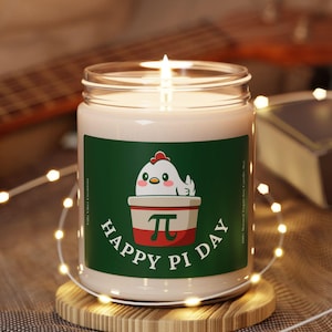 May include: A white candle with a green, red, and white label. The label features a cartoon chicken holding a pie with the text "Happy Pi Day".
