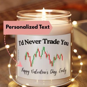 May include: A scented candle in a clear glass jar with a white label featuring the text I'd Never Trade You, a red and green stock market candlestick chart graphic, and the text Happy Valentine's Day, Emily, resting on a round wooden base.