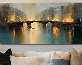 May include: An abstract landscape painting depicting a bridge over a body of water, with buildings on either side. The artwork features warm golden and cool teal tones, creating a serene and atmospheric scene. The painting is displayed above a white sofa.