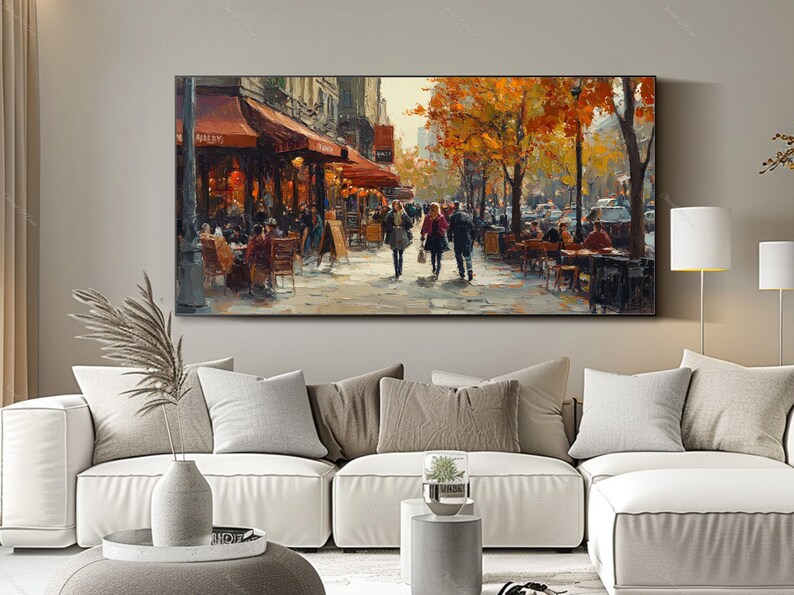 May include: A painting of a Parisian street scene with people walking and sitting at outdoor cafes. The buildings are painted in warm tones, and the trees are in autumn colors. The painting is framed in a black frame.