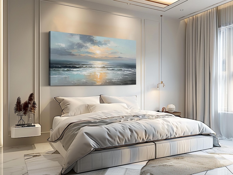 Op de afbeelding: Een slaapkamer met een groot bed, wit beddengoed en een grijze sprei. Boven het bed hangt een landschapsschilderij van een zeegezicht met een zonsondergang. De kamer heeft witte muren, een wit tapijt en lichtgekleurde gordijnen.