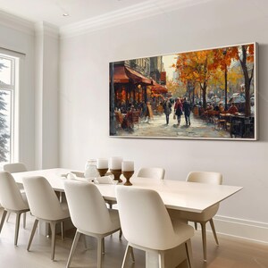 May include: A painting of a Parisian street scene with people walking and sitting at outdoor cafes. The painting is framed and hanging on a white wall above a white dining table with white chairs.