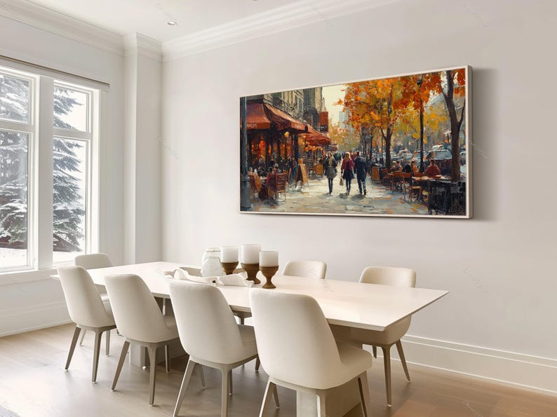 May include: A painting of a Parisian street scene with people walking and sitting at outdoor cafes. The painting is framed and hanging on a white wall above a white dining table with white chairs.