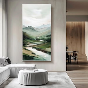 May include: Vertical landscape painting depicting a mountain valley with a river. The artwork features shades of green, brown, and white, creating a serene and natural scene. The painting is displayed in a modern living room setting.