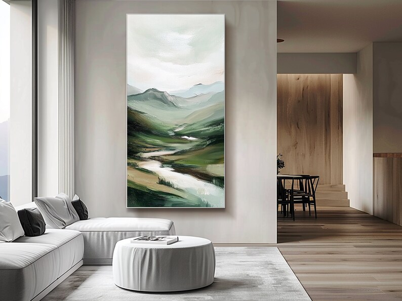 May include: Vertical landscape painting depicting a mountain valley with a river. The artwork features shades of green, brown, and white, creating a serene and natural scene. The painting is displayed in a modern living room setting.