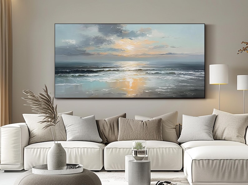 Op de afbeelding: Grote rechthoekige canvas kunst die een zeegezicht bij zonsondergang uitbeeldt. Het schilderij toont een mix van blauw, grijs en oranje, met zichtbare penseelstreken. Het kunstwerk is zwart omlijst en hangt boven een witte bank.