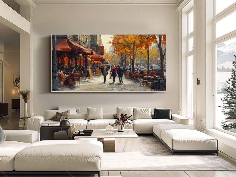 May include: A painting of a Parisian street scene with people walking and sitting at outdoor cafes. The buildings are painted in warm tones, and the trees are in autumn colors. The painting is framed and hanging on a wall.