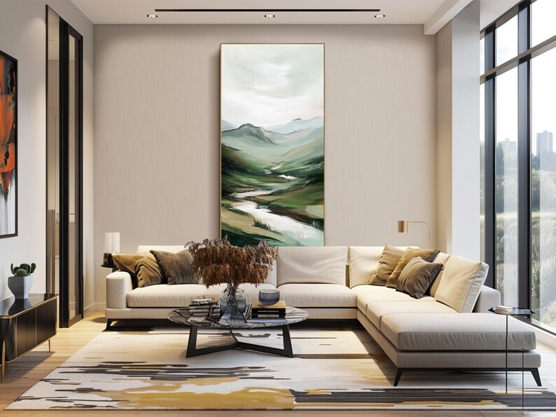 May include: An interior shot of a modern living room with a large, abstract landscape painting. The painting features green and white brushstrokes depicting a valley and river. A white sectional sofa, a patterned rug, and a marble coffee table complete the scene.