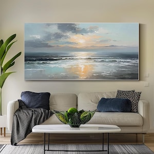 Op de afbeelding: Olieverfschilderij van een zeegezicht met zonsondergang. De lucht is gevuld met grijze en witte wolken en de zon gaat onder boven de oceaan. De golven slaan op de kust en het water weerspiegelt de kleuren van de lucht. Het schilderij hangt boven een beige bank.